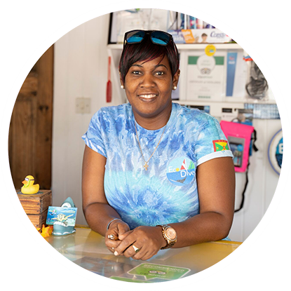 A woman in a blue shirt is smiling at a table after scuba diving in Grenada.