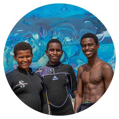 Three boys in wetsuits, ready for a Grenada snorkeling adventure, standing in front of a mural.