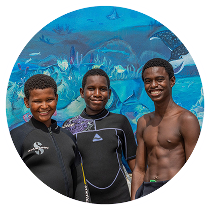 Three boys in wetsuits, ready for a Grenada snorkeling adventure, standing in front of a mural.