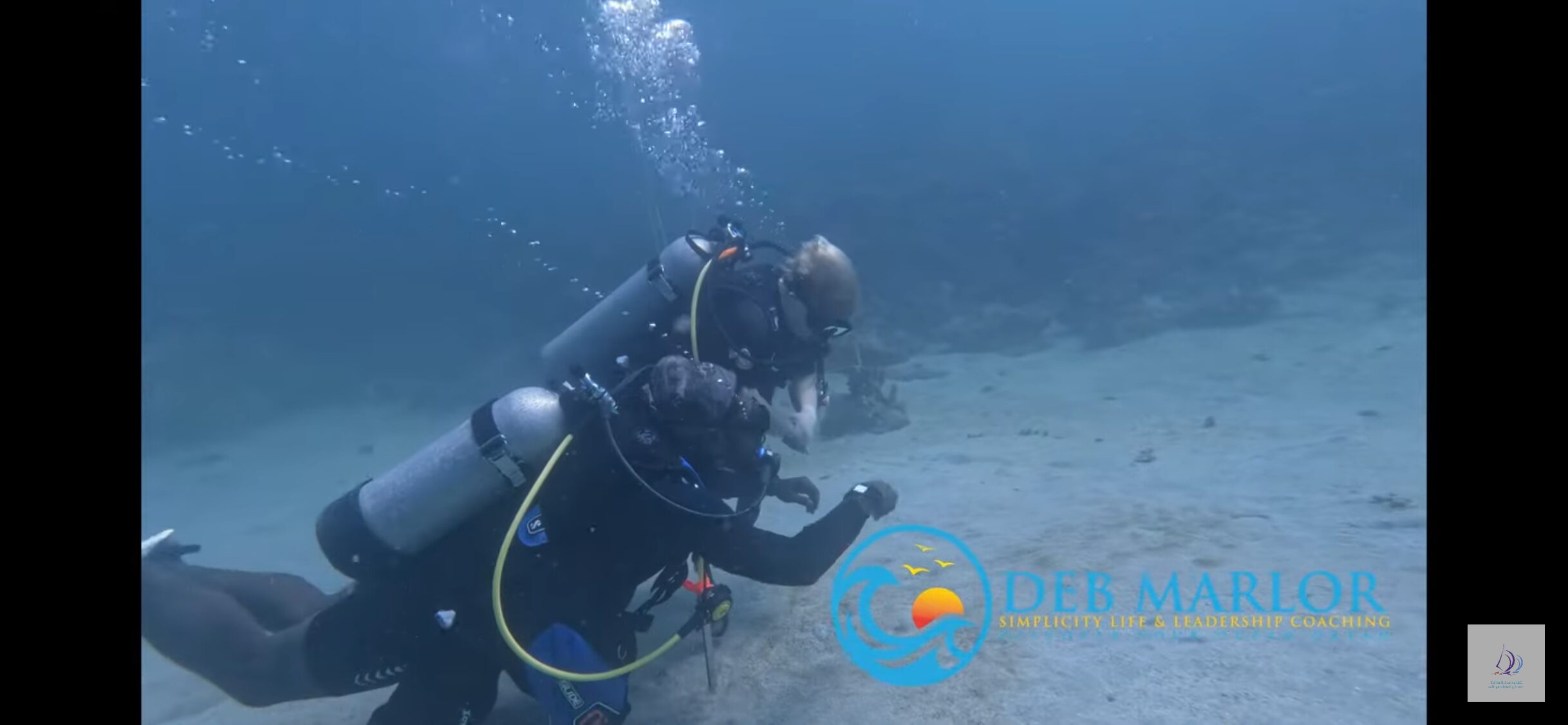 Two scuba divers underwater with bubbles rising from their equipment. The background is the ocean floor. Logo and text for Deb Marlor Simplicity Life & Leadership Coaching appear in the lower right corner, helping you achieve your scuba goals like Kelly does.
