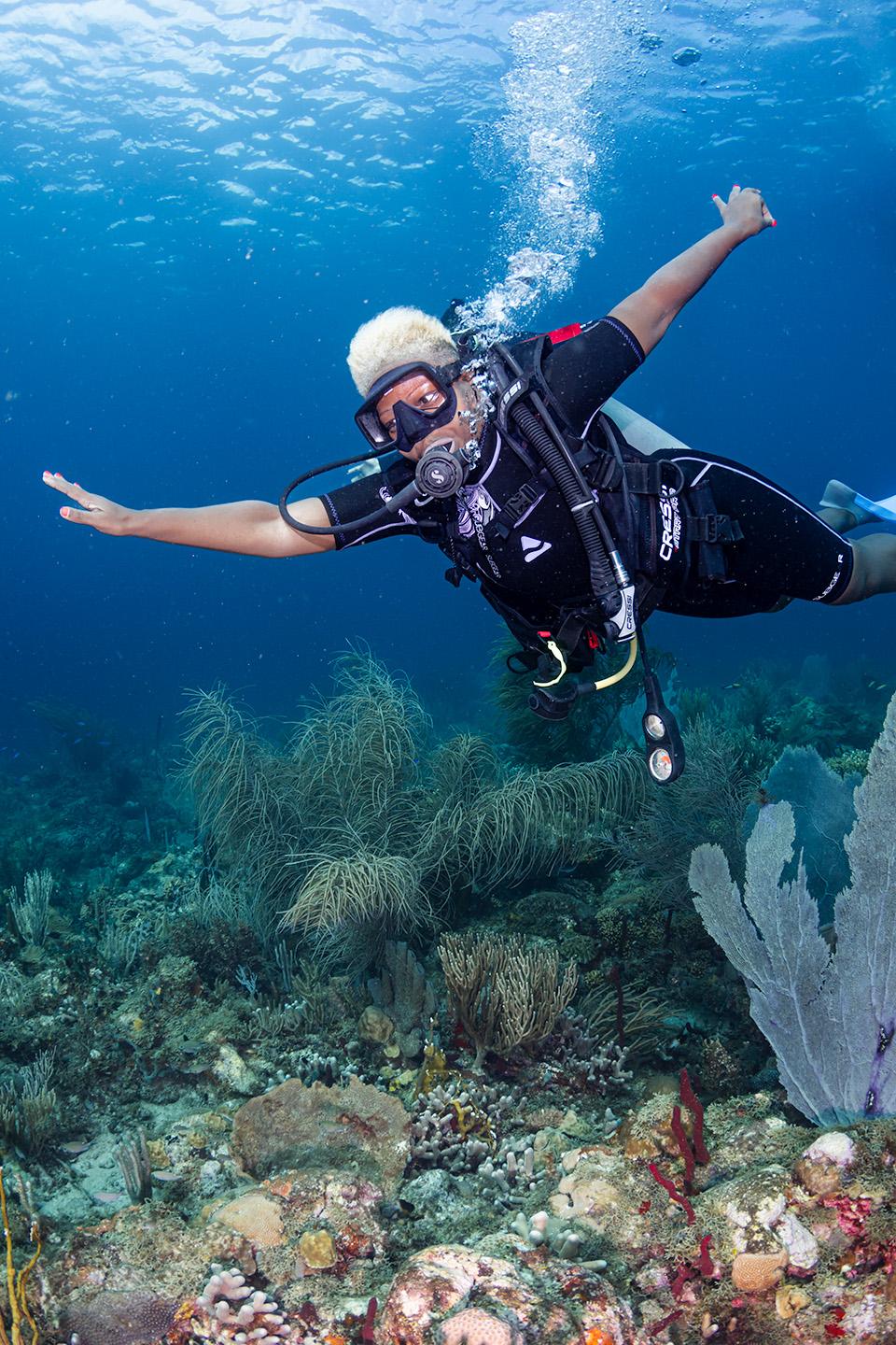 Scuba diver in full gear gliding over a colorful coral reef in clear blue water to celebrate Grenada's 50th anniversary.